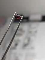 Front view of loose oval red spinel held in tweezers