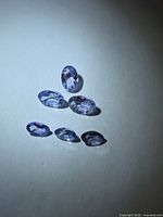 Six loose oval purple tanzanites under direct light