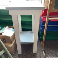 Full view of tall white accent table showing top, legs, and lower shelf