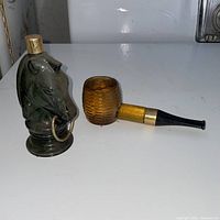 Green glass horse head decanter beside amber pipe bottle