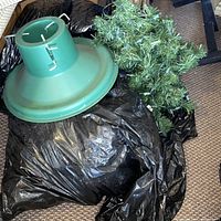 Green plastic Christmas tree stand, artificial greenery on black bag
