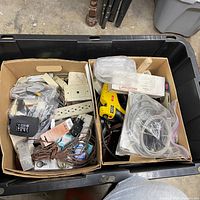 Overall view of plastic tote with two cartons of cords, power strip, yellow drill, adapters visible