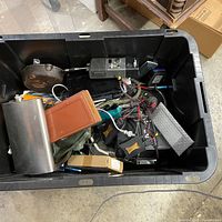 Overall view of bin with electronic items, cords, adapters, flask, cast-iron pan