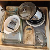 Drawer contents showing glass bakeware, mixing bowls, lids, grater, cutting board