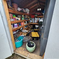Wide view of shed interior showing tools on shelves, toolbox, plastic tubs, planter