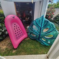 Pink Ozark Trail lounger and teal leaf float leaning against shed