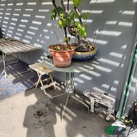 Green metal bistro table with potted plants, folding stand, additional table in background