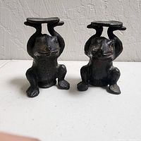 Front view of pair of cast iron frog candle holders showing platforms and patina