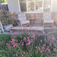 Front porch view showing two wooden rocking chairs with patterned cushions, glass side table between them, wooden bench in foreground