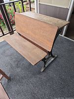 Full view of wooden school desk with cast iron sides and attached bench
