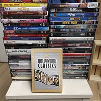 Two tall stacks of assorted DVD cases with Hollywood Classics 50-movie pack in front