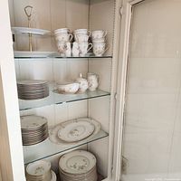 Cabinet shelf showing stacked plates, cups, sugar bowl, creamer and dessert stand