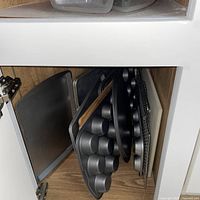 Stacked metal bakeware, cutting board and cooling rack in lower cabinet