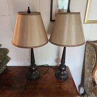 Two matching bronze metal table lamps with beige shades on wooden surface