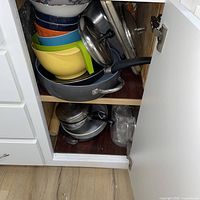 Cabinet shelf showing nested plastic bowls, ceramic bowl, sauté pan, fry pan handle, and lids