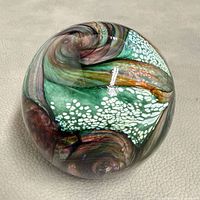 Full view of spherical paperweight showing swirled colors and mottled white pattern