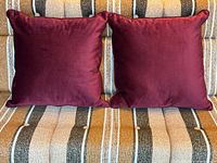 Front view of both burgundy velvet pillows on striped sofa