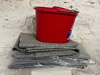 Red Vileda bucket stacked on folded and packaged grey felt underlays
