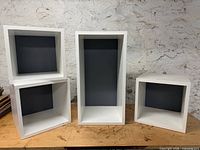 Front view of four white modular cubes showing three square and one rectangular with grey backs