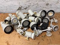 Pile of approximately twenty white and black-trim track lighting heads on workbench