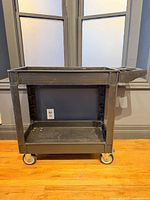 Full view of black plastic two-shelf cart on casters