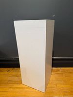 Full view of white painted wood pedestal against wall