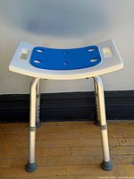 Front view of white shower seat showing blue pad and adjustable legs