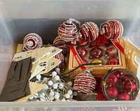 Overview of lot inside plastic bin showing ornaments, paper village pieces, garland, boxed ornaments