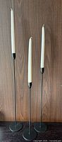Three black metal candle holders with white candles displayed together