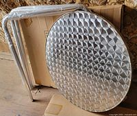 Unassembled round aluminum tabletop and wrapped legs on shipping box