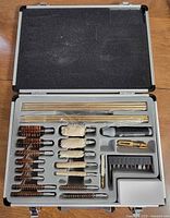 Open case showing full cleaning kit components arranged in foam insert: brass rods, brushes, mops, handle, jags, patch compartment