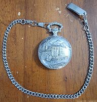 Front of pocket watch showing embossed semi-truck design and attached chain