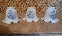 Front view of three identical milk glass lamp shades displaying blue floral design and ruffled edges