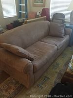 Three-seater brown fabric sofa with rolled arms and two matching pillows, placed in a living room setting.