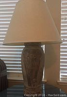 Elephant-shaped table lamp standing on a table near window blinds, beige tapered shade on top.