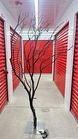 Full view of tall black painted manzanita LED tree on metal base in storage unit