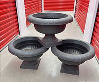 Three black resin pedestal urn planters stacked for scale and quantity