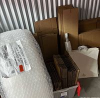 Lot showing stacked box flats, bubble wrap roll, stretch wrap roll, paper bags