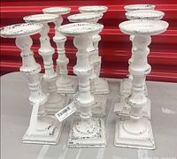Group of nine matching white distressed metal candlesticks on surface