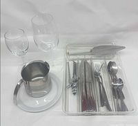 Full lot overview showing flatware in tray, cake server, can opener, creamer on plate and two wine glasses