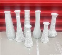 Seven white milk glass vases lined up showing varied patterns and heights
