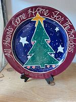 Front view of hand-painted Christmas plate on stand showing inscription, tree design, date