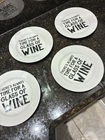 Four identical white plates with black wine quote displayed on countertop