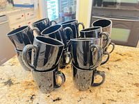 Group of twelve black ceramic mugs stacked on countertop