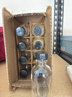 Front view of cardboard box showing glass bottles and one bottle outside