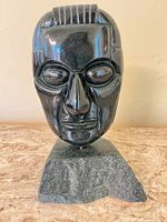 Front view of polished stone bust on base showing facial details and top grooves