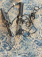 Two curling irons with cords on patterned rug