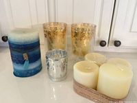 Group shot of pillar candle, two gold floral votive holders, silver votive holder, pack of ivory votives
