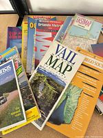 Stack of various folding maps showing titles such as Vail Walking Map, FastMap Chicago, Rand McNally Orlando Metro, Arkansas State Highway Map