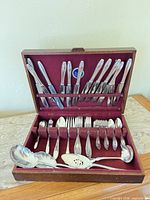Full flatware set in open wooden chest showing knives, forks, spoons and serving pieces